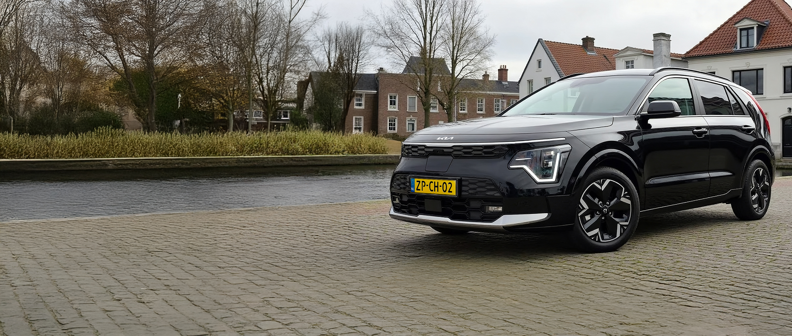 Kia Niro EV geparkeerd op een plein voor een huis met een laadpaal.