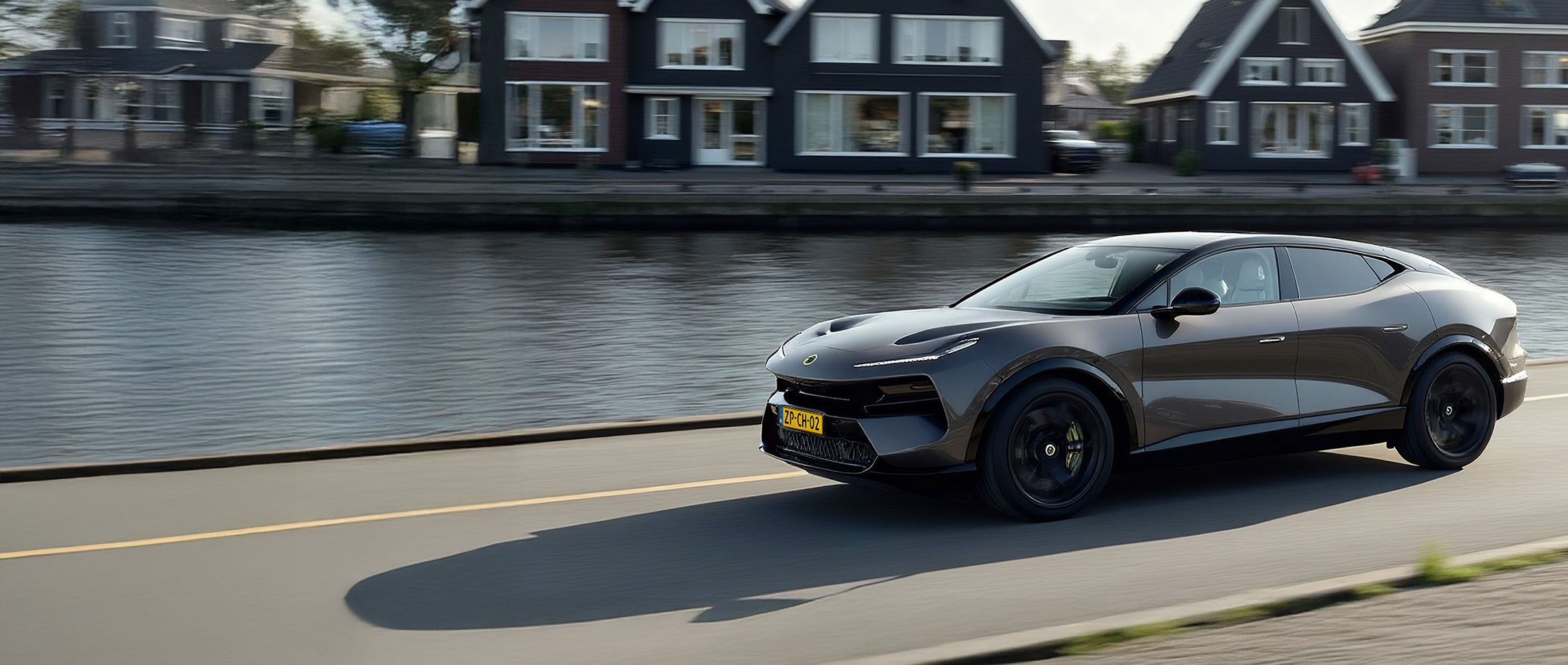 Lotus Eletre rijdend langs huizen aan het water, met een laadpaal op de oprit.