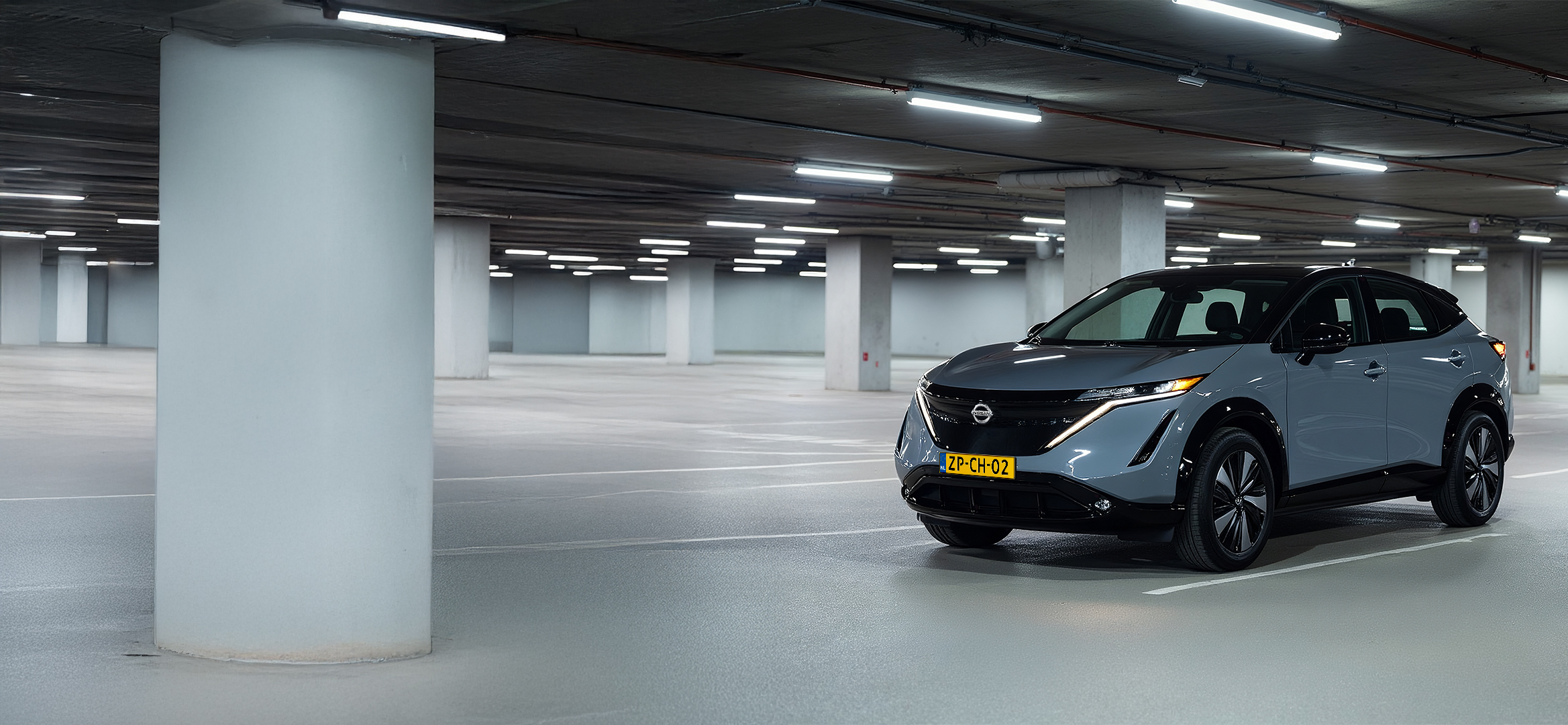 Een elektrische Nissan Ariya staat geparkeerd in een parkeergarage terwijl hij oplaadt aan een laadpaal.