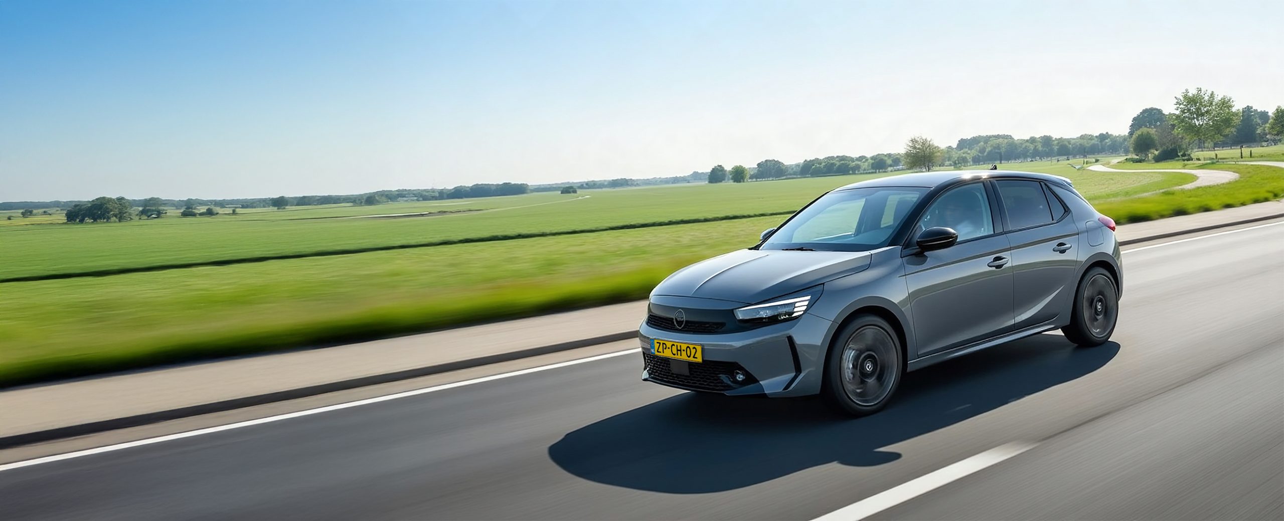 Een Opel Corsa Electric rijdt in een Nederlands landschap. Onderweg naar huis om de auto op te laden aan de laadpaal.