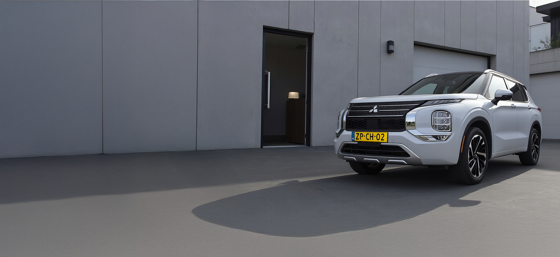 Een Mitsubishi Outlander geparkeerd naast een loods. De elektrische auto staat op te laden aan de laadpaal.